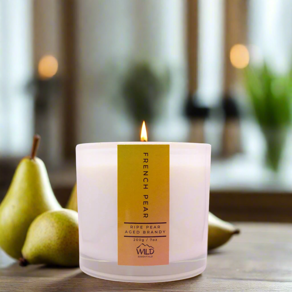 Photo of the French Pear Luxury Candle handcrafted by Wild Essentials. Photo taken in a modern kitchen with wooden cabinetry with pears nearby.