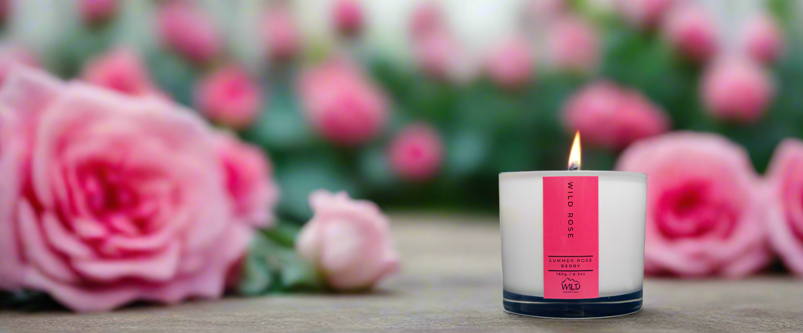 Photo of the Wild Rose candle from Wild Essentials. In the background pink Roses can be seen.