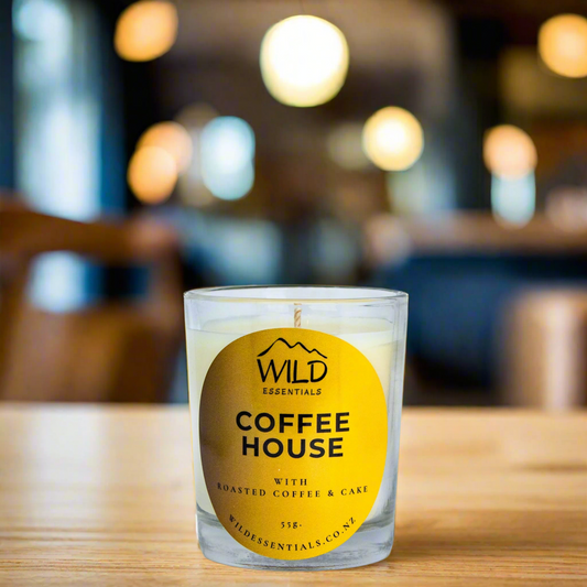 Photo of the Coffee House Mini Candle made by Wild Essentials. It is on a wooden table in a warmly lit Cafe.
