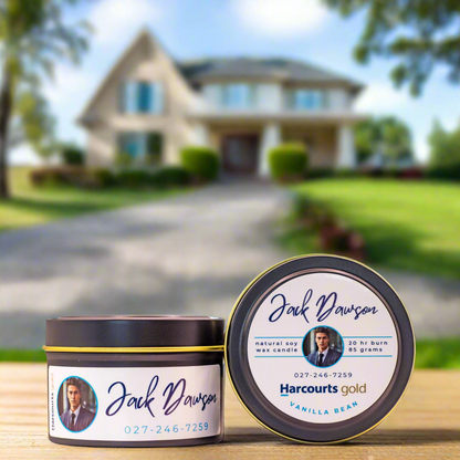 Photo of a 85g Real Estate Custom Candle from Wild Essentials. Black candle tin, white label. A house can be seen in the background.