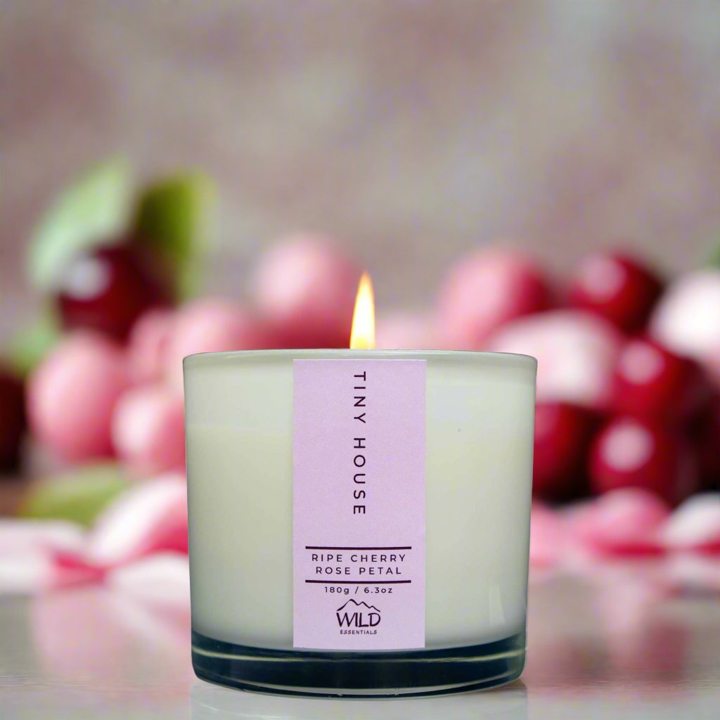 Photograph of the Luxurious Tiny House Aromatherapy Candle by Wild Essentials with scents of Ripe Cherry and Rose Petal with background.